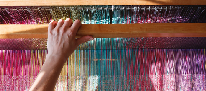 Close-up of a hand weaving colorful threads on a loom.