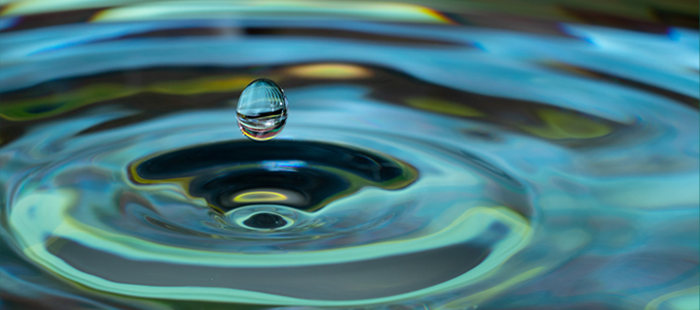 Close-up view of water drop in blue/green water and its outward ripples