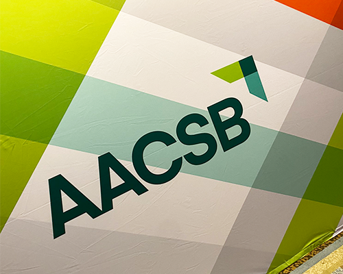 AACSB corporate mark, without tagline, printed on multicolor weave background on display at the 2023 ICAM conference
