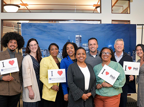 Nine PhD Project members attending ICAM 2023, holding up signs that say "I [heart] PhD Project"