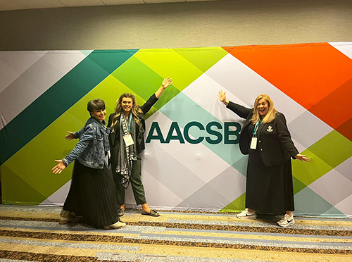 Photo of three ICAM 2023 attendees standing in front of colorful AACSB banner