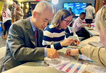 Oliver Yao, dean of the Lerner College of Business and Economics, sits at a table with faculty and students choosing letter beads out of a small plastic container to make a friendship bracelet as part of an informal networking event for the Data Enchanted workshop series