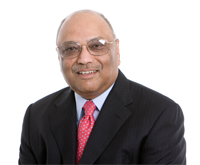 Professional headshot of C.K. Prahalad, influential business strategist and former professor at the University of Michigan Ross School of Business. He is smiling and has brown eyes, a slight graying moustache and brows, and high hairline. He wears mid-size oval wire-frame glasses, a dark pinstripe suit, a white shirt, and a red patterned tie and sits against a white background. 