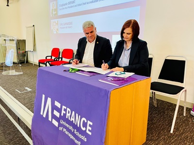Éric Lamarque of IAE France and Stephanie Bryant of AACSB sign a memorandum of understanding at a table with a purple tablecloth